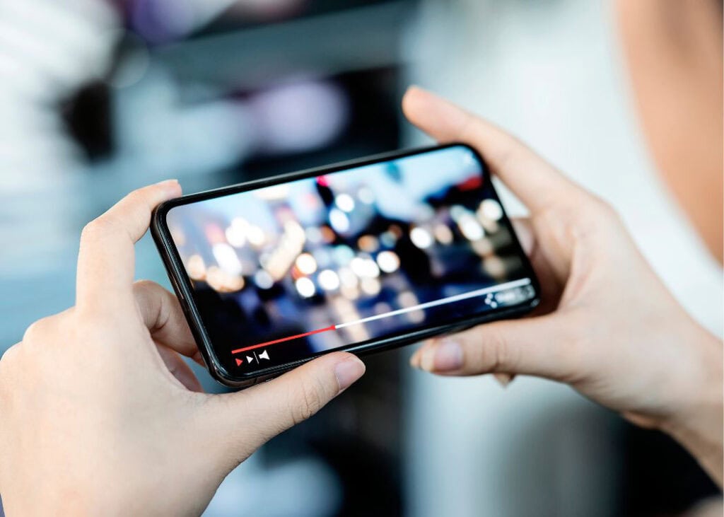 Hands holding smartphone displaying video with blurred lights.