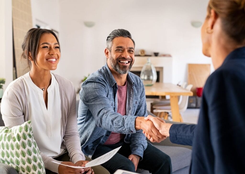 Couple shaking hands with advisor in living room.