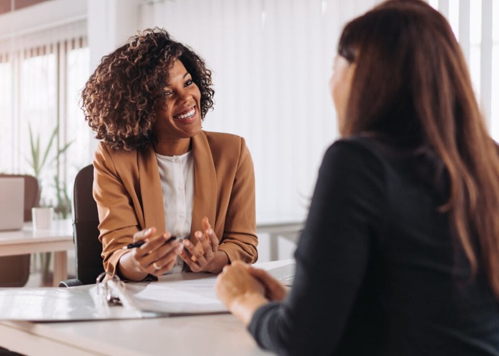 Two women smiling, discussing business in modern office.