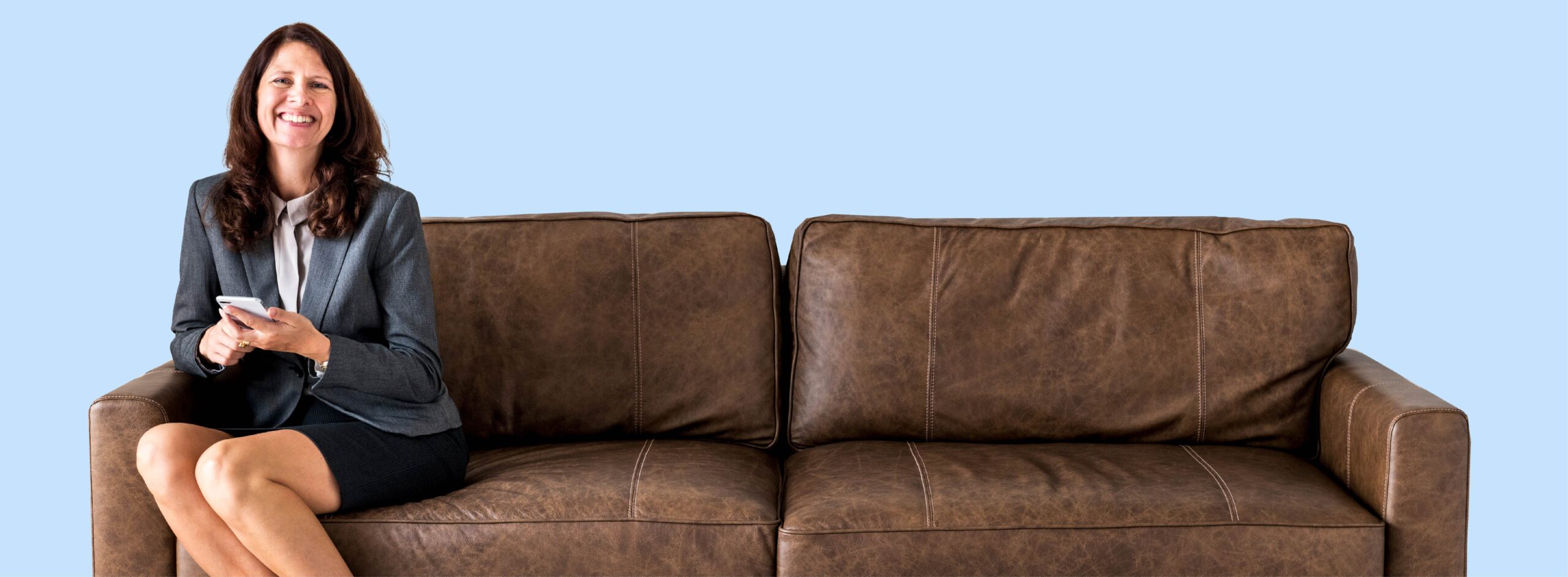 Smiling woman with phone sitting on brown leather couch.