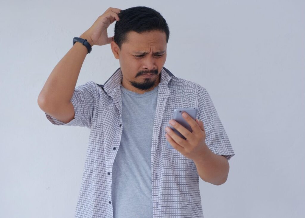 Confused man looking at smartphone, scratching head.