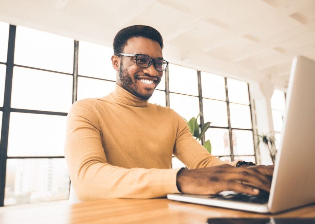 Smiling man using laptop in sunny office.