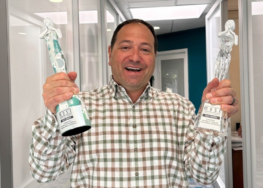 Man smiling, holding two design award trophies.