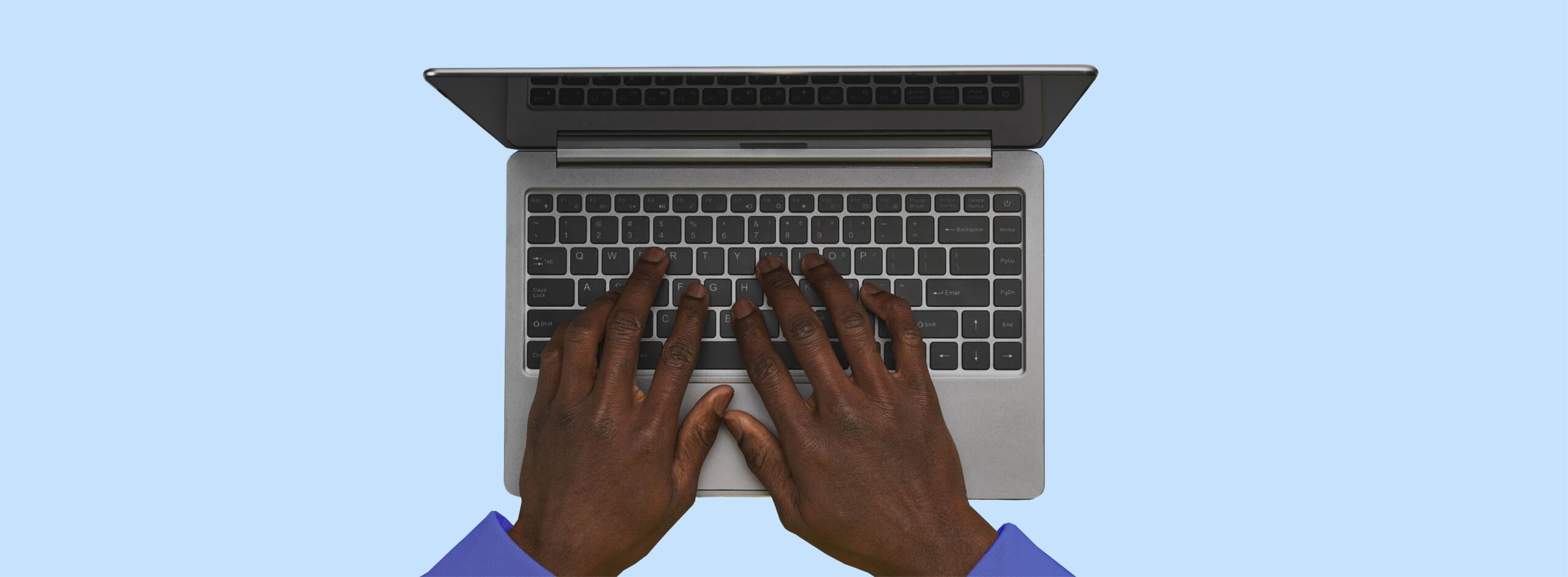 Hands typing on laptop keyboard, blue background.