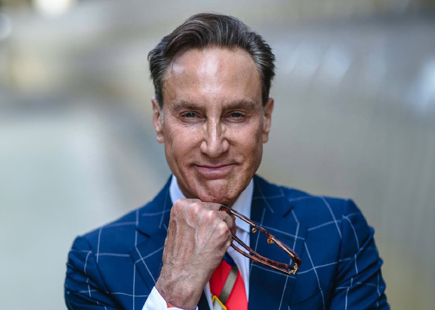 Confident businessman smiling, holding glasses, in blue suit.