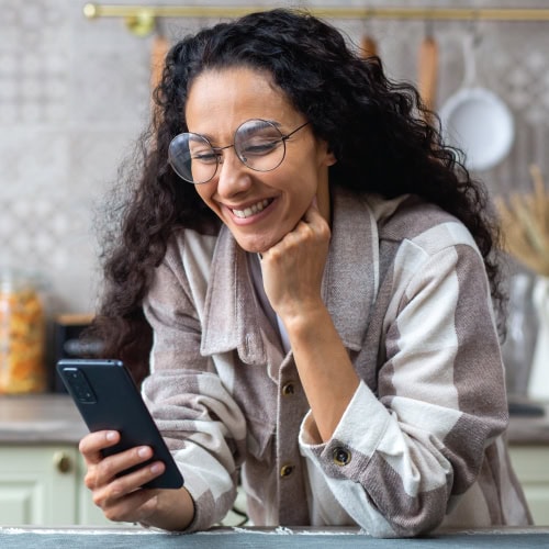 Woman smiling at smartphone in kitchen.