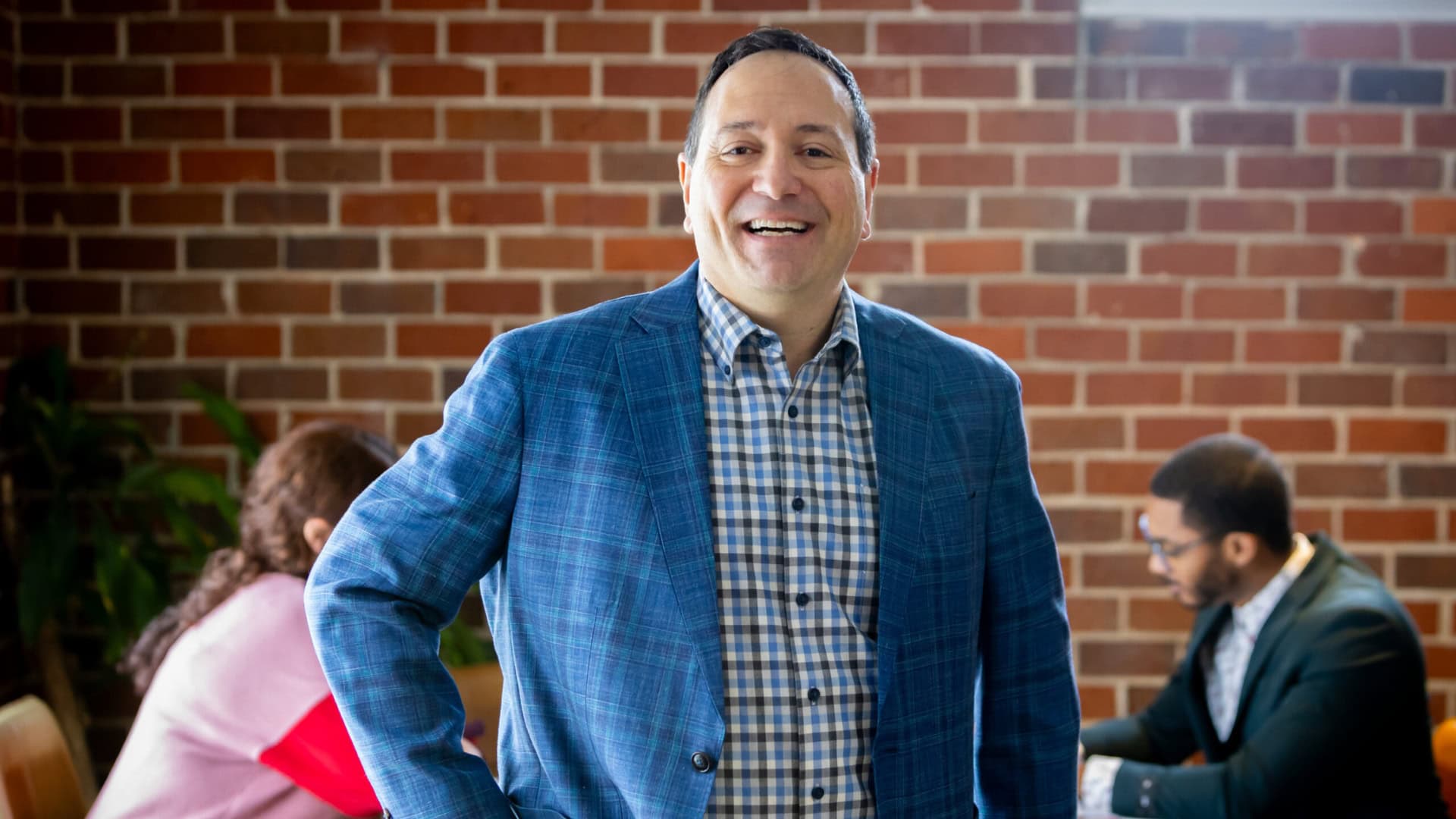 Smiling businessman in office with colleagues in background.