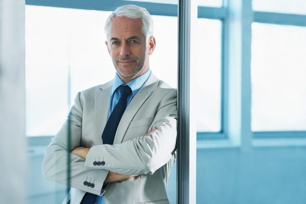 Confident senior businessman leaning on office window.