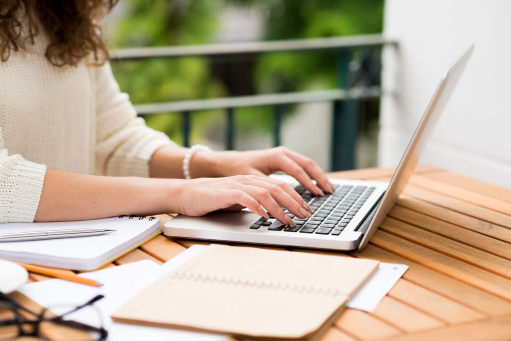 Woman typing on laptop at outdoor table.