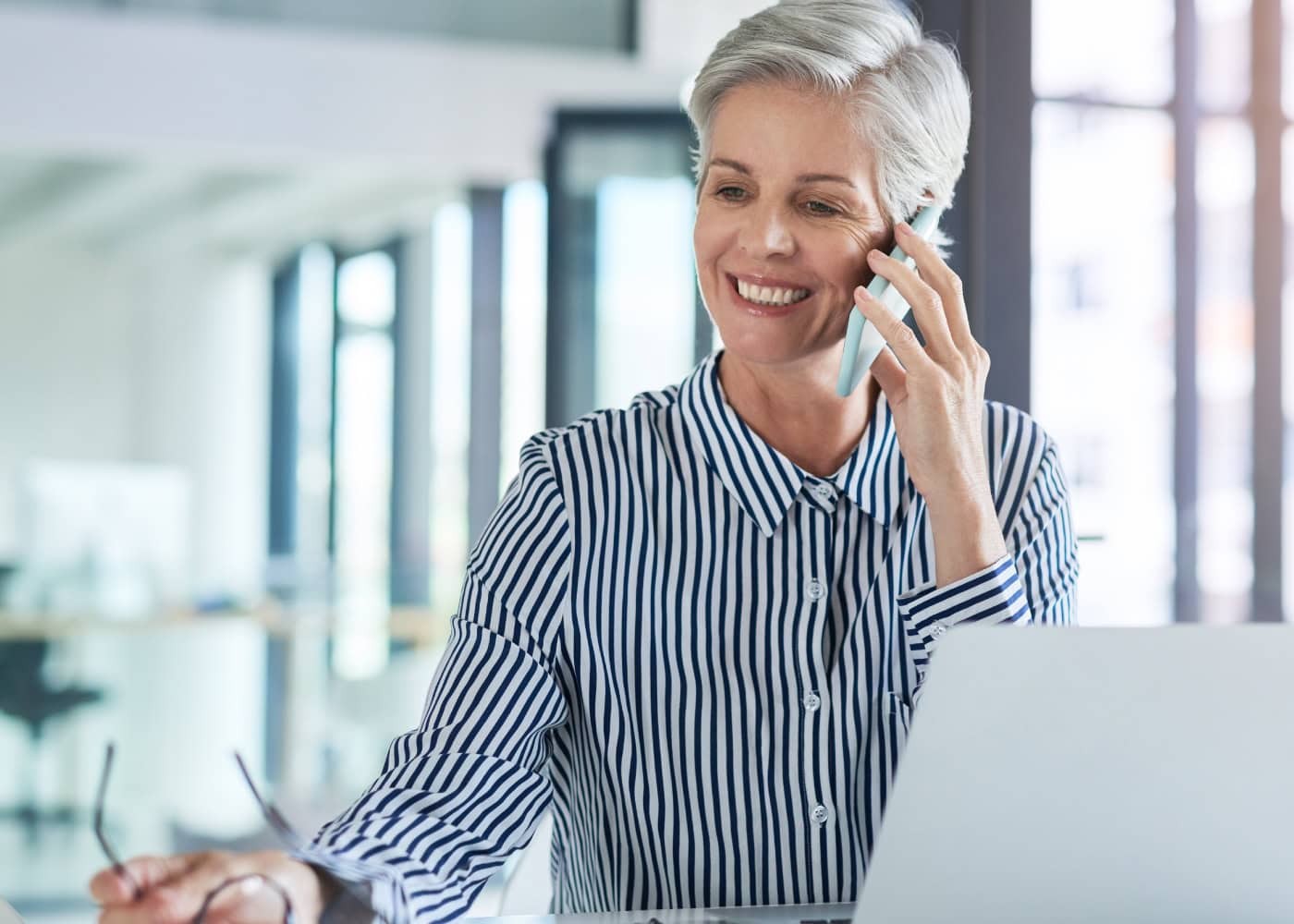 Senior businesswoman smiling while talking on phone at desk.