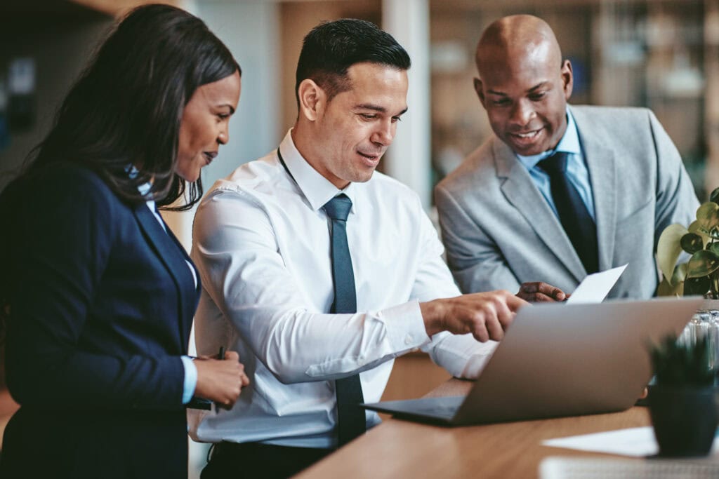 Three professionals collaborating at a laptop in office.