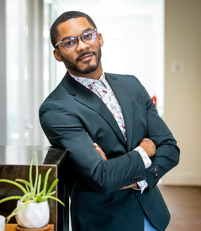 Confident businessman in office with glasses and green suit.