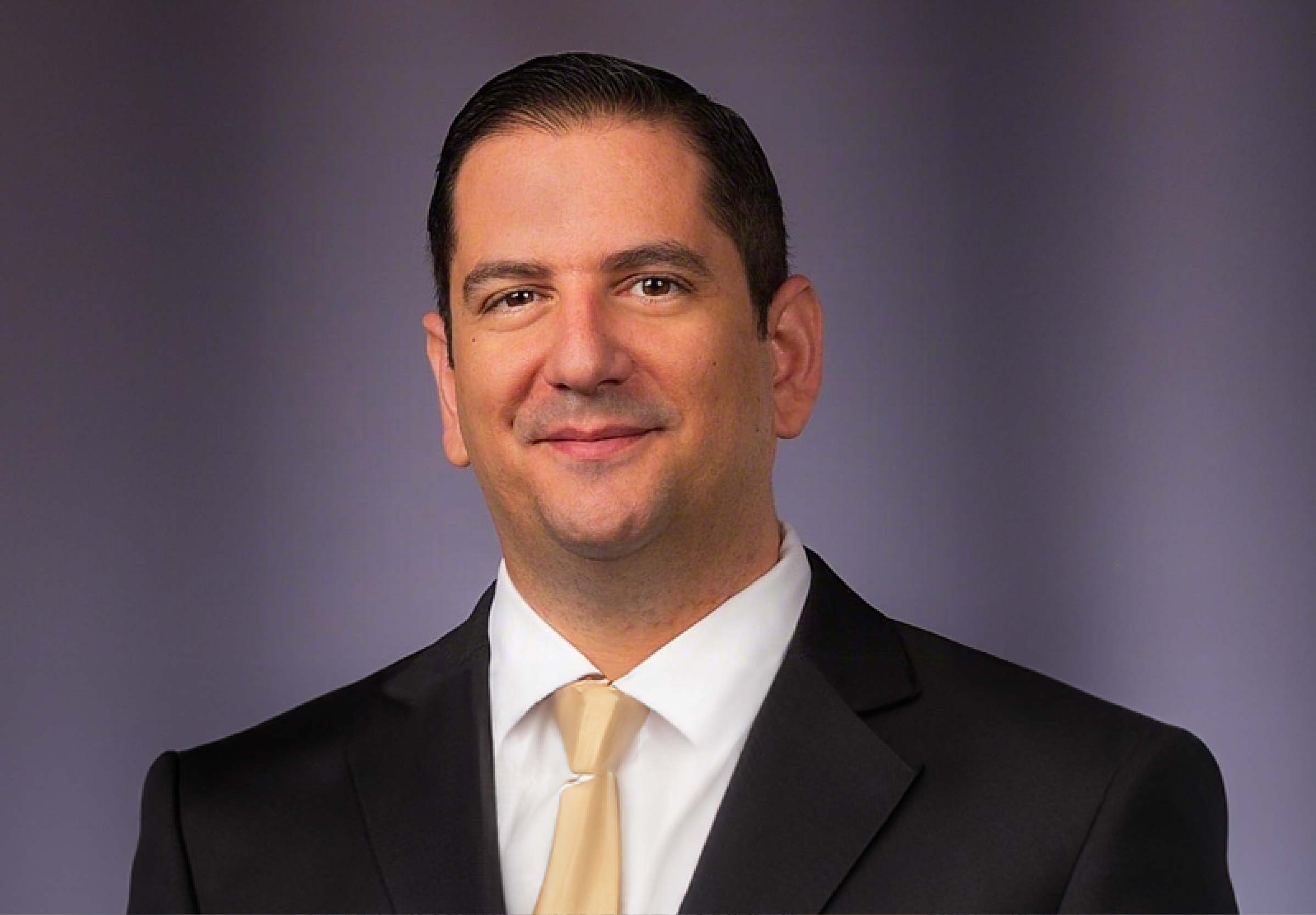 Professional man in suit smiling, neutral background.