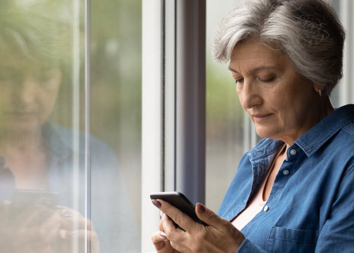 Senior woman using smartphone near window.