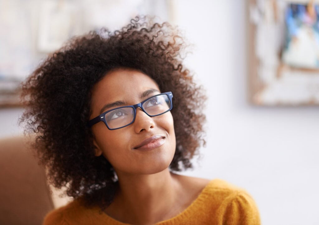 Thoughtful Black woman wearing glasses, looking away.