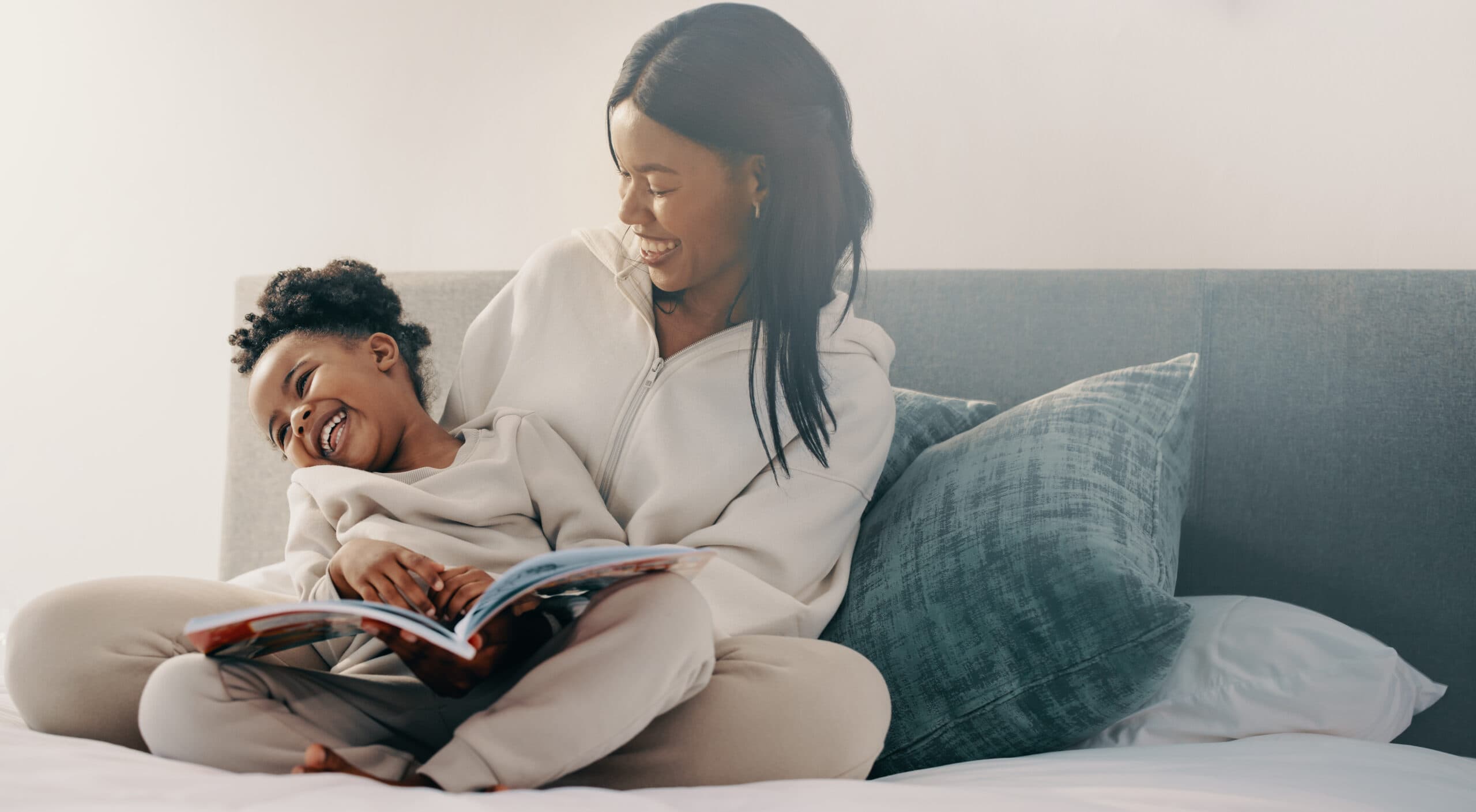 Mother and child laughing while reading book on bed