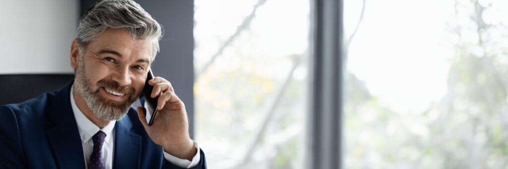 Smiling businessman talking on phone by office window