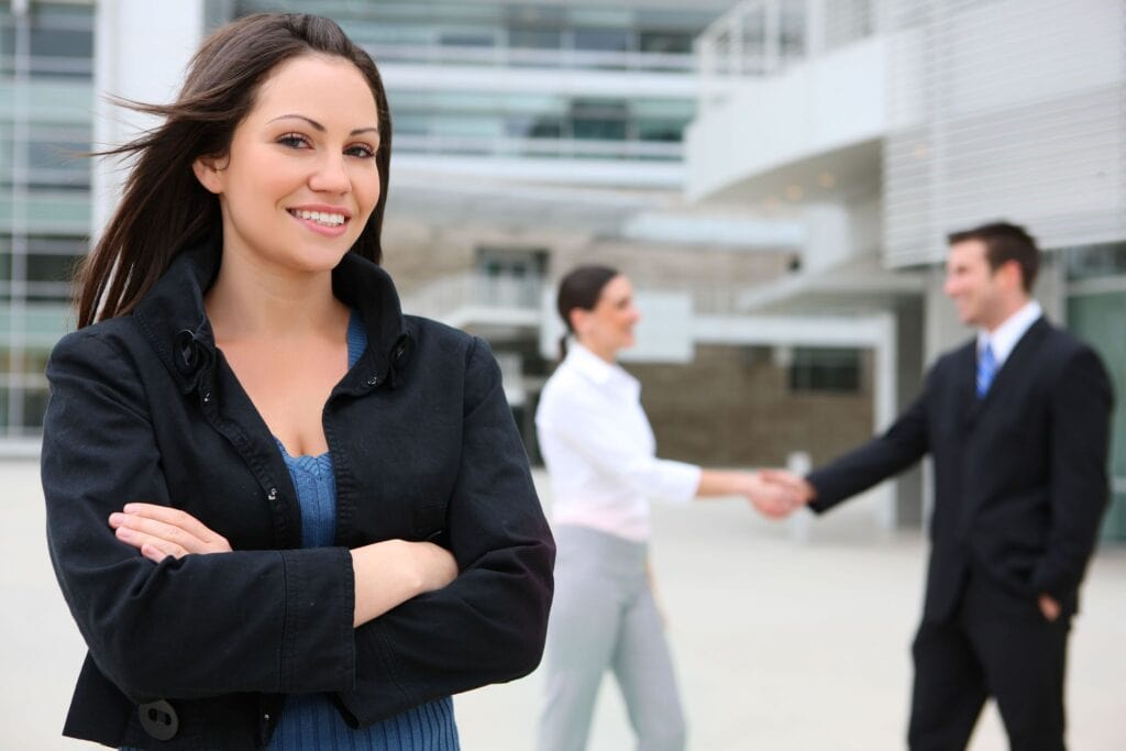 Confident woman with colleagues shaking hands in background