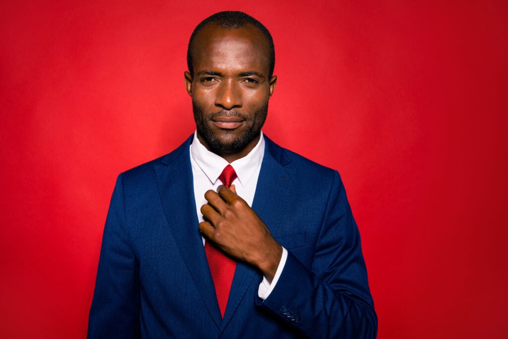 Man in blue suit adjusting tie on red background