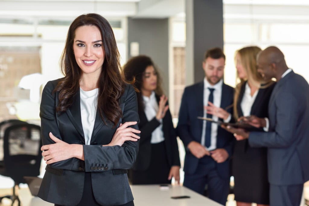 Confident businesswoman with team discussing in background