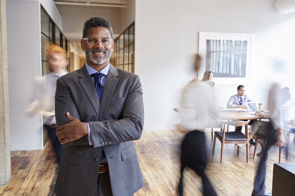 Confident businessman with arms crossed in busy office