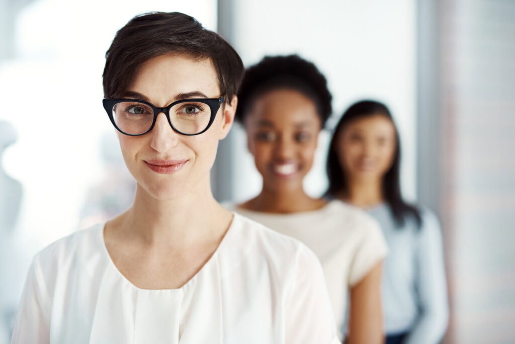 Confident professional woman with glasses, colleagues blurred behind
