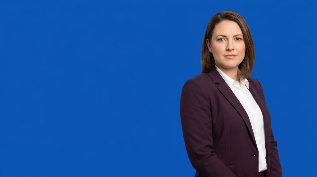Asian woman professional in her late 30s, average build, dark plum blazer and white shirt, on a blue studio background — Criminal Defense Law Firm Marketing: How to Reach Clients Who Need You Right Now.