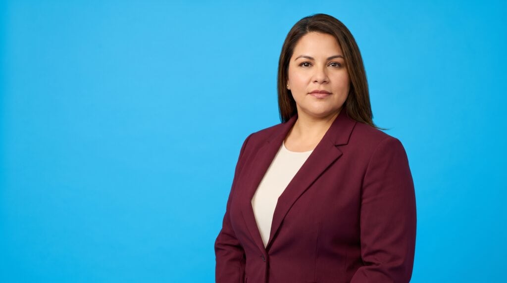 Hispanic woman professional in her late 30s to 40s, curvy build, burgundy blazer and cream top, on a blue studio background — Answer Engine Optimization for Law Firms: The Complete Guide.